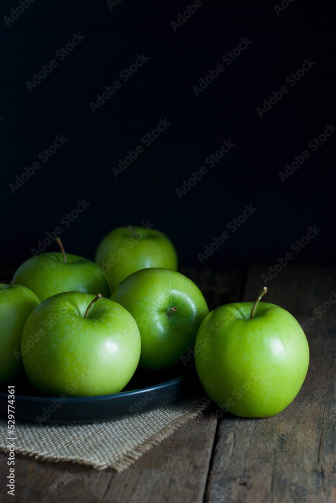 Delicious green apples in a black ceramic tray put on sackcloth on a rustic wooden floor. Delicious green apples in a black ceramic tray put on sackcloth on a rustic wooden floor.
