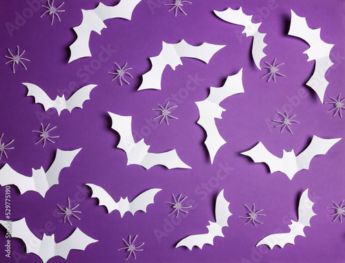 Halloween flat lay composition with white bats and spiders on purple background.