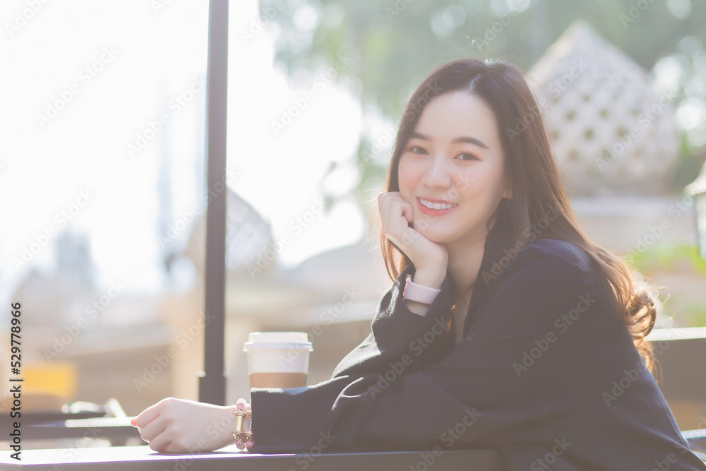 Beautiful business Asian woman in a dark blue suit is sitting on chair to drink coffee and smiling happily in front of the cafe  near the office on a sunny morning.