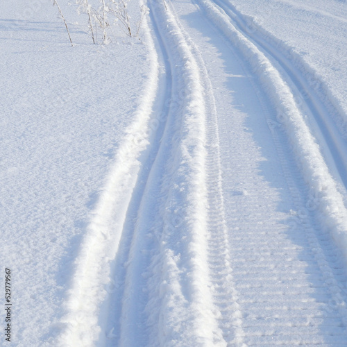 Track of traces from a snowmobile in drifts of white snow. Nature and outdoor on a winter sunny day. Square illustration with snowy field © Deacon docs