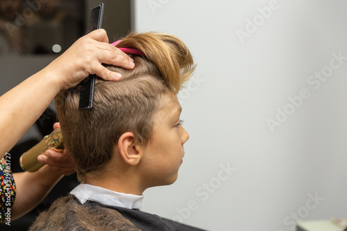 Nice european boy getting hairstyle in barbershop.