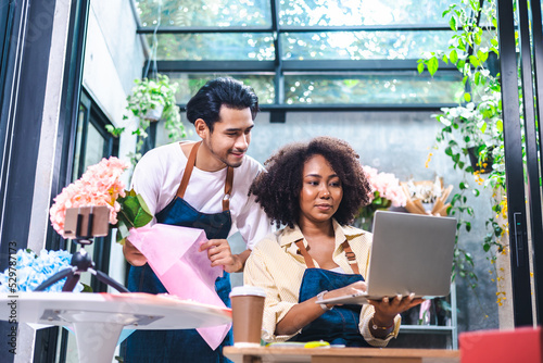 Asian male and  African female florists flower store owners working and doing inventory. Man typing on laptop at desk in floral shop . Business concept