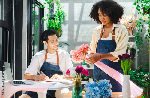 Asian male and  African female florists flower store owners working and doing inventory. Man typing on laptop at desk in floral shop . Business concept
