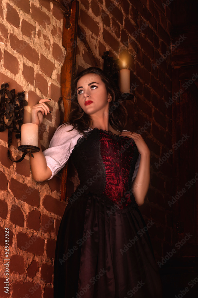 Fantastic medieval woman in the night castle. Anticipation, fear, anticipation. Royal velvet vintage red dress with fur and gold, princess, queen, brunette with long hair. Castle, dusk, night, luxury