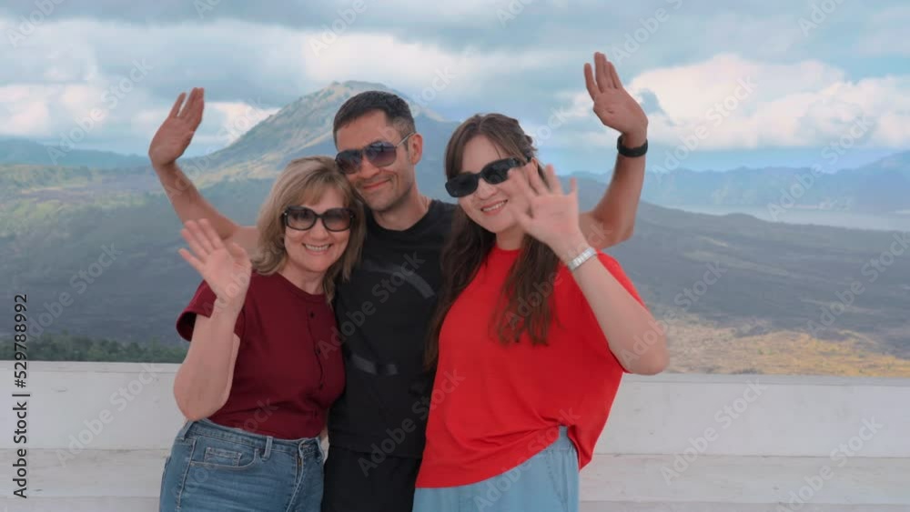 Happy family smiling and waving to camera against beautiful Mountain View. Tourists posing in front of valley and volcano during summer vacation trip Group of asian European people smiling slow motion Happy family smiling and waving to camera against beautiful Mountain View. Tourists posing in front of valley and volcano during summer vacation trip Group of asian European people smiling slow motion