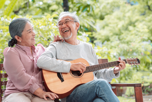 Happy Asian senior couple elderly man playing guitar music song enjoy having fun happiness outside house near backyard garden. Retirement insurance concept © Kiattisak