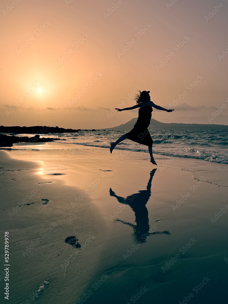 Silhouetted girl dancing at sunset on sandy beach by the ocean reflected in water at playa del Risco, Lanzerote, Canary Islands