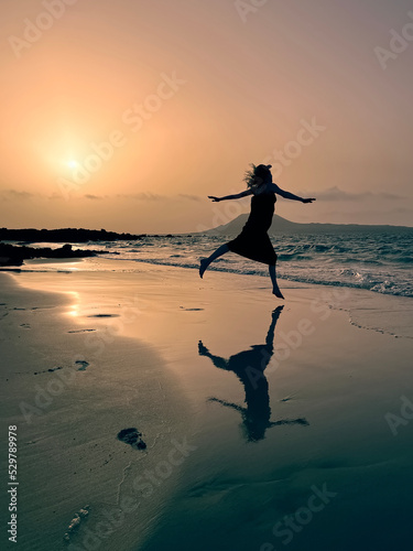 Obraz na płótnie Silhouetted girl dancing at sunset on sandy beach by the ocean reflected in water at playa del Risco, Lanzerote, Canary Islands w salonie