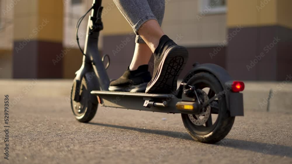 Girl rides an electric scooter. Child travel cheerfully. Empty city street. Legs on an electric scooter. Girl travel on scooter. Child on deserted street. Electric scooter close up. City travel girl