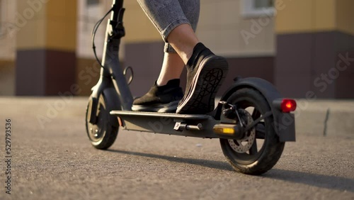 Girl rides an electric scooter. Child travel cheerfully. Empty city street. Legs on an electric scooter. Girl travel on scooter. Child on deserted street. Electric scooter close up. City travel girl