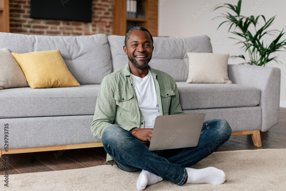 Smiling middle aged african american guy in casual typing on laptop, have video call, chat in social networks