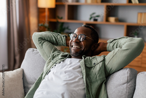 Satisfied adult african american man in glasses and casual resting and relaxing, enjoy comfort, peace and free time photo