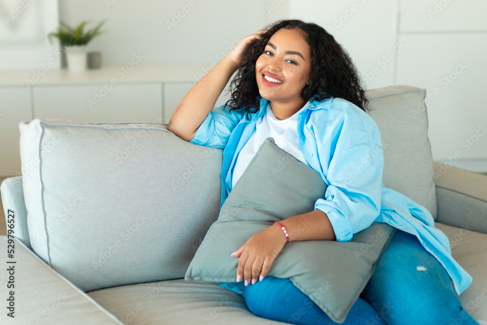 Happy African Lady Sitting On Sofa Holding Pillow At Home Happy African Lady Sitting On Sofa Holding Pillow At Home