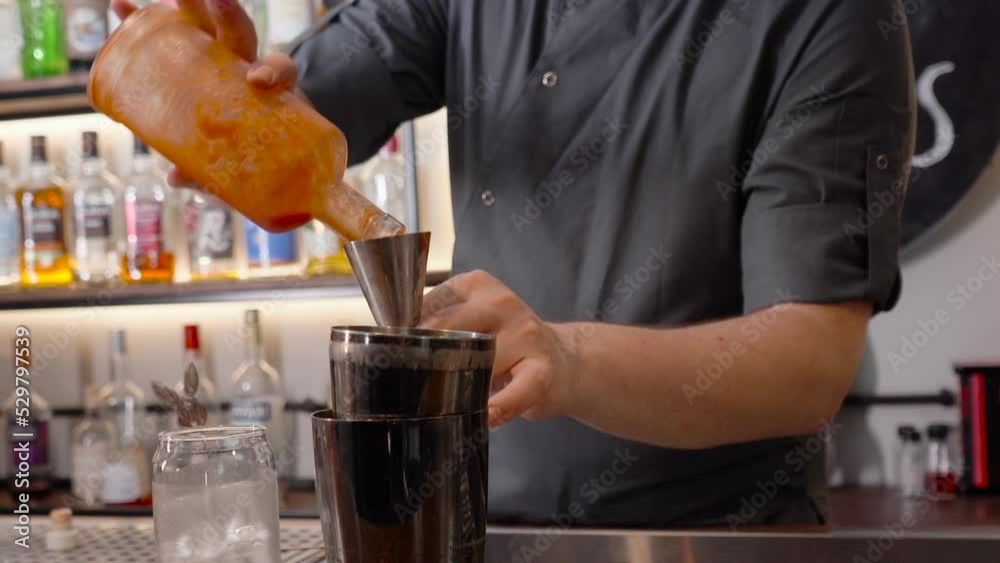 A bartender measures and pours alcohol liquor from jigger to a cocktail shaker. A bartender measures and pours alcohol liquor from jigger to a cocktail shaker.