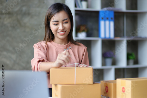 Shipping shopping online, young woman starts up small business owner writing address on cardboard box. Small business entrepreneur SME or freelance Asian woman working with parcel box at home. © Wasan