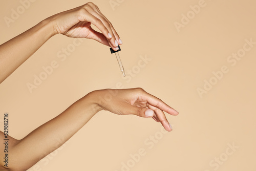 Moisturizing skin of hands with essential oil or serum. Woman applying essential oil to her hands with pipette dropper on beige background