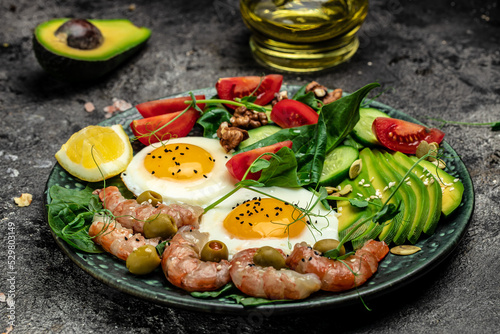 shrimps, prawns, soft fried egg, fresh salad, tomatoes, cucumbers and avocado on a dark background. Ketogenic diet breakfast. Keto, paleo lunch. Long banner format. top view