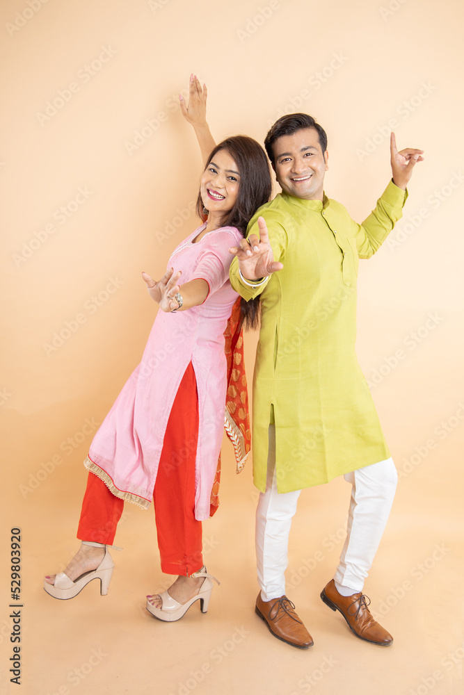 Happy indian couple dancing together wearing traditional or ethnic cloths isolated on studio background, Man and woman celebrating diwali festival, online shopping deal, enjoying life concept, Happy indian couple dancing together wearing traditional or ethnic cloths isolated on studio background, Man and woman celebrating diwali festival, online shopping deal, enjoying life concept,