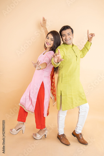 Happy indian couple dancing together wearing traditional or ethnic cloths isolated on studio background, Man and woman celebrating diwali festival, online shopping deal, enjoying life concept, © gajendra