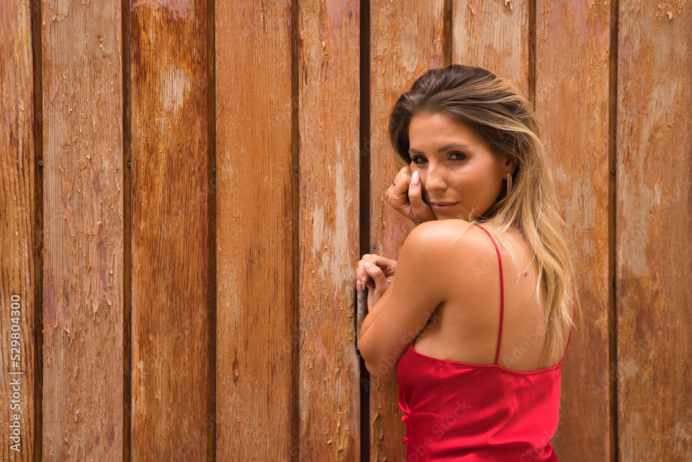 Portrait of young, attractive, blonde woman, wearing an elegant red party dress, with sensual look, on a background of wooden planks. Concept beauty, fashion, elegance, luxury, sensuality. Portrait of young, attractive, blonde woman, wearing an elegant red party dress, with sensual look, on a background of wooden planks. Concept beauty, fashion, elegance, luxury, sensuality.