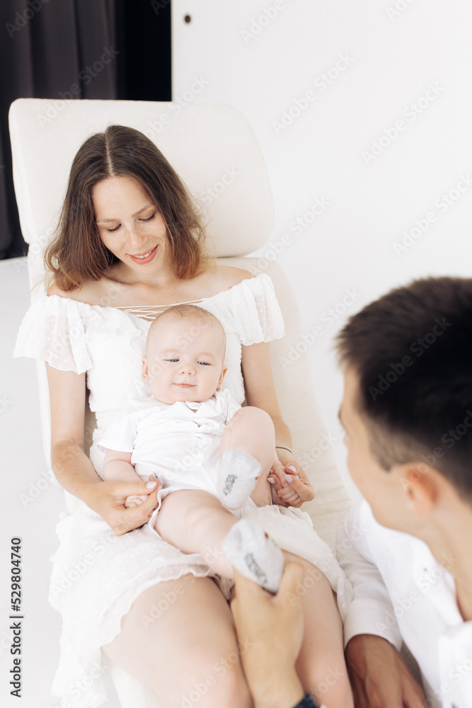 Young happy parents sit in armchair and play with their baby boy. Young happy parents sit in armchair and play with their baby boy.