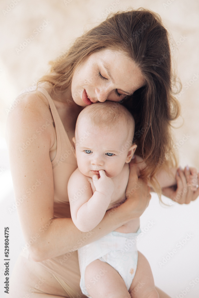 Happy mother in bodysuit sits and embraces her baby. Happy mother in bodysuit sits and embraces her baby.