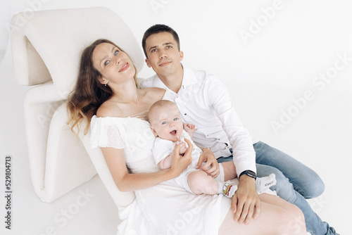 Young happy parents sit in armchair and play with their baby boy.