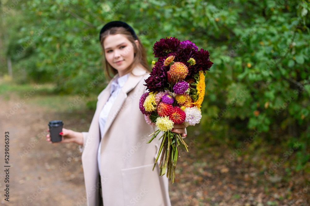 Fototapeta premium Autumn bouquet of flowers and a cup of tea in the hands of a cute girl
