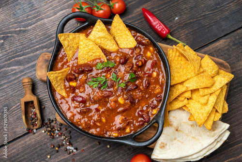 Mexican food chili con carne dish with corn chips nachos on a wooden backdrop. Bean and corn soup, red bean stew