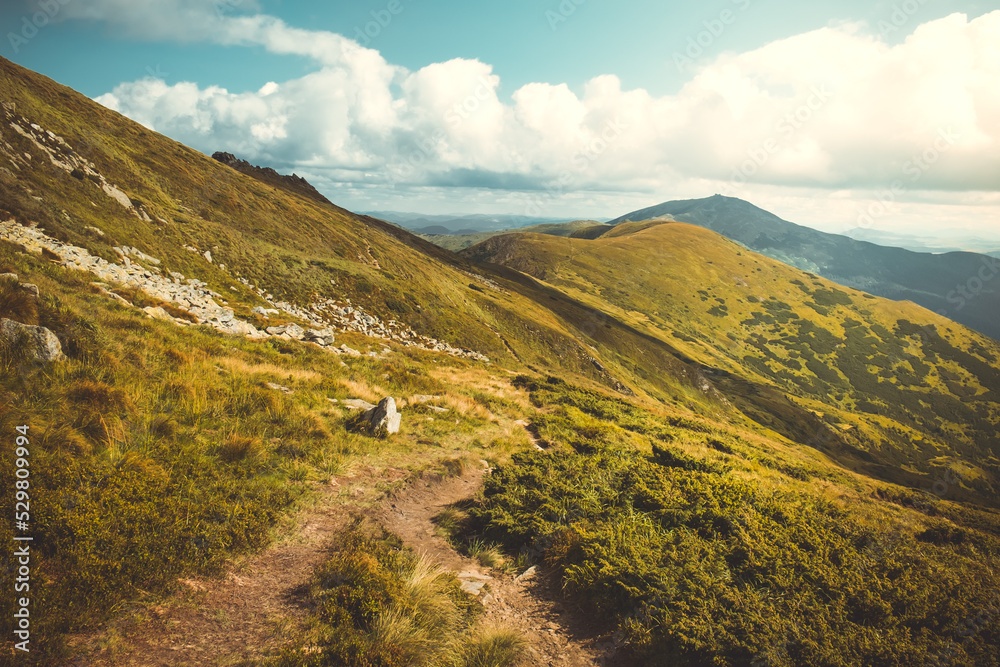 Autumn mountain nature landscape. Tourist trail along orange grass hills and mountain range. Panoramic view of beautiful alpine landscape. Travel, hiking, freedom, active lifestyle. Vintage retro tone Autumn mountain nature landscape. Tourist trail along orange grass hills and mountain range. Panoramic view of beautiful alpine landscape. Travel, hiking, freedom, active lifestyle. Vintage retro tone