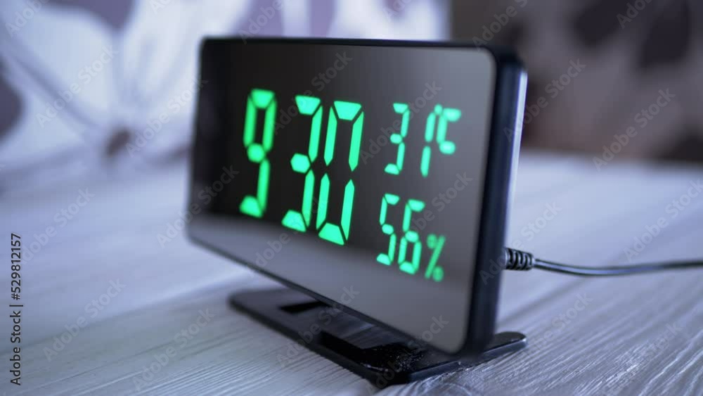 Digital Clock Showing Time on Green Display 9:30 AM, Temperature, Air Humidity. Modern mirror clock, alarm clock with a thermometer, hydrometer standing on a desk on white background. Time concept.