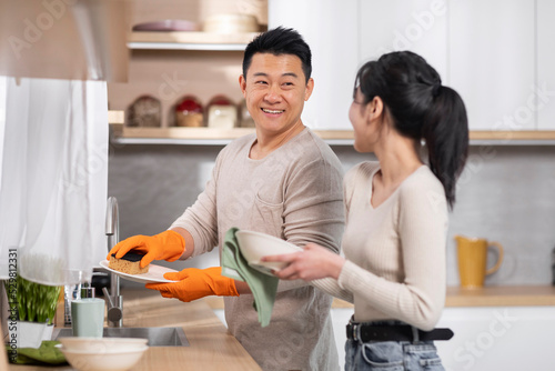 Cheerful asian spouses doing chores together, washing dishes