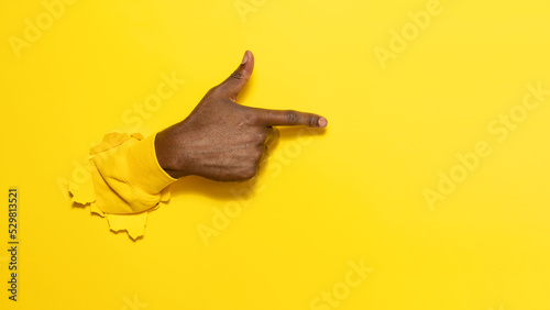 Fototapeta Naklejka Na Ścianę i Meble -  African american male hand pointing aside on virtual object or text, gesturing through the torn yellow paper background