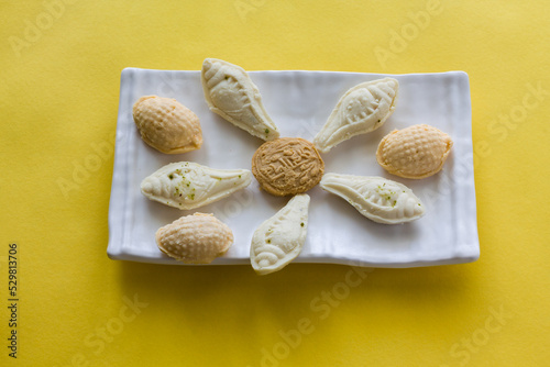 Variety of Sandesh or Sondesh ,a Bengali Sweet or Indian dessert served in a white plate and isolated on yellow background. Made of cottage cheese, sugar or jaggery. photo