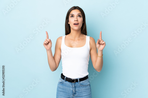 Young caucasian woman isolated on blue background surprised and pointing up