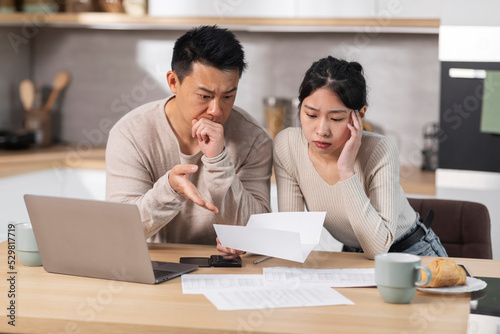 Unhappy asian husband and wife reading letter, kitchen interior © Prostock-studio