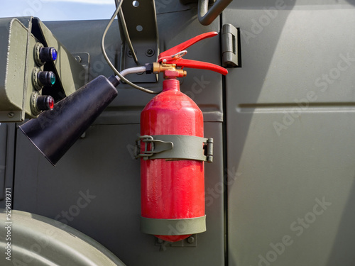 Fire extinguisher is fixed on car body. Flame extinguishing equipment. Carbon dioxide fire extinguisher hangs on metal mounts. Carbon dioxide fire extinguisher to protect equipment from ignition