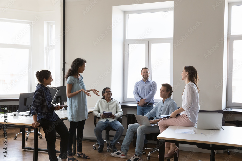 Young multiethnic business team brainstorming in project, sharing creative ideas for startup on meeting in office, sitting, standing in circle, talking, smiling, laughing