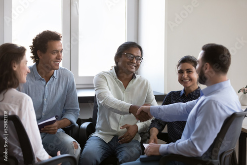 Happy diverse business colleagues men shaking hands with gratitude, recognition, respect. Multiethnic group therapy friends giving handshakes on meeting, talking, laughing, smiling © fizkes