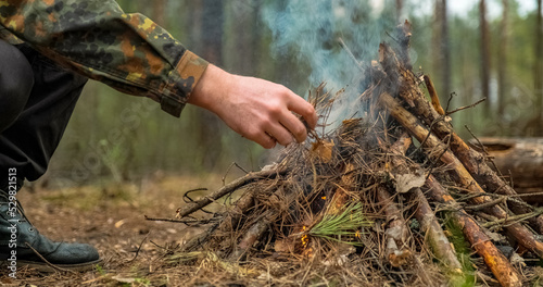 Low angle shot of a man is trying make a fire in the forest. Close-up of a man's hand lighting a campfire. Lighting a fire in the forest by a person. Low angle of a burning fire made of brushwood.