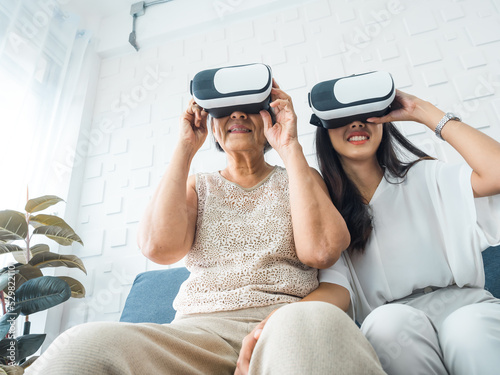 Asian old senior woman, mother and happy young daughter, female wearing VR glasses, enjoy 3d game online together in white room. Mom and daughter with reality virtual technology lifestyle concept.