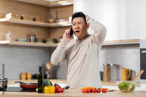 Wallpaper Mural Shocked asian man cooking meal and talking on phone Torontodigital.ca