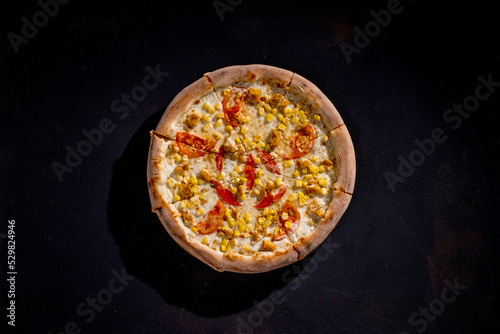 Pizza for children on a cream base with chicken fillet, tomatoes, corn and mozzarella cheese on black background