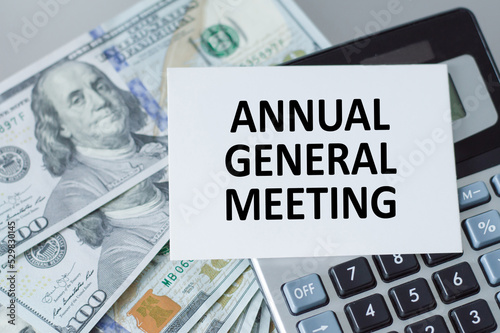 Business and finance concept. On the table there is a clock, a pen, a calculator and a business card on which the text is written - ANNUAL GENERAL MEETING