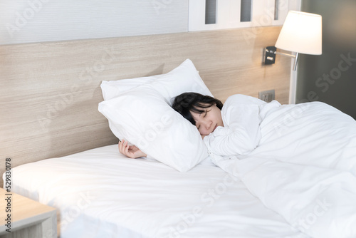 Asian cute young woman in white long arm pajamas lie on her side on the bed