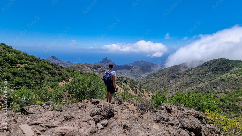 Man with backpack enjoying panoramic view on the Teno mountain massif seen from summit Pico Verde, Tenerife, Canary Islands, Spain, Europe. Hiking trail between Masca and Santiago. Wanderlust vibe