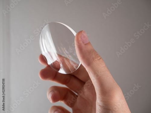 Quadro su tela Hand holds a glass eyeglass prescription lens in the laboratory