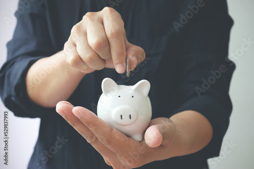 Man hand holding piggy bank and putting coins in piggy bank for saving money and plan finance. Save money and financial investment concept.