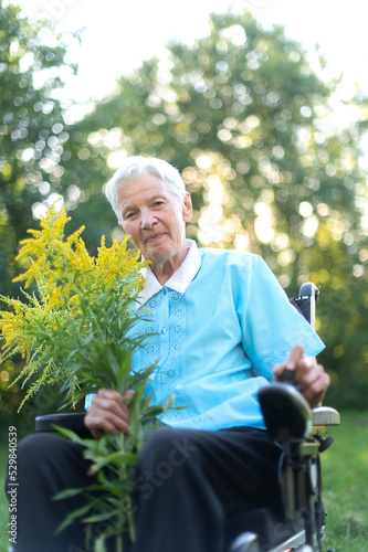 happy old senior woman sitting in a wheelchair and holding a bouquet of yellow wildflowers
