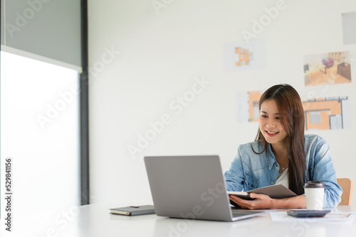 Construction design concept, Female architect taking notes while working about house plan on laptop